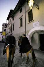 Una coppia di cavalieri percorre una stadina lungo i portici.